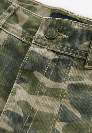 Camo-patterned fabric in shades of green and beige with visible stitching. Features a metal button at the waist, denim texture.