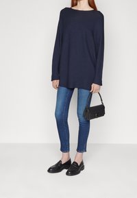 Maglione oversize color navy, jeans skinny blu, mocassini neri e una piccola borsa nera con manico. Tessuto morbido, vestibilità comoda.