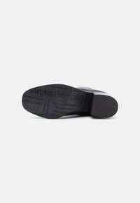 Suola di scarpa nera realizzata in gomma testurizzata con nome del marchio e dettagli impressi. Tacco arrotondato e design minimale, bordi lisci.