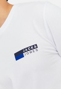 Weißes Baumwoll-T-Shirt mit einem großen navyblauen und blauen "JACK & JONES"-Logo auf der linken Brust, glatte Textur und V-Ausschnitt-Design.