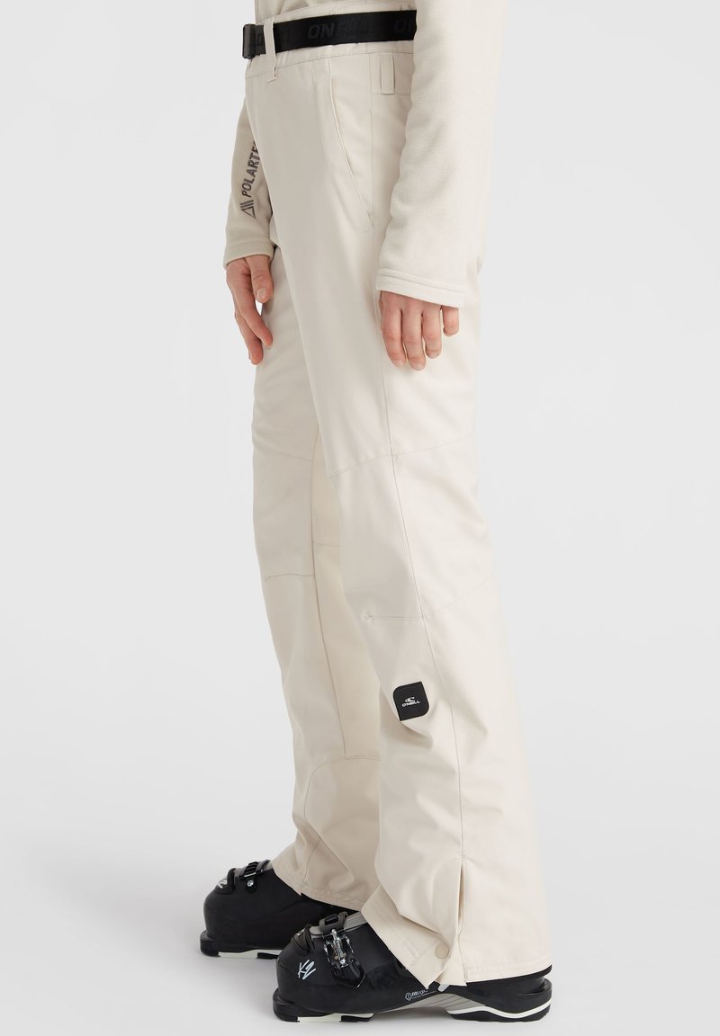 Pantalones de esquí beige con un diseño ajustado, costuras visibles y un parche con el logo en el muslo. Presentan una cinturilla duradera y puños ajustables.