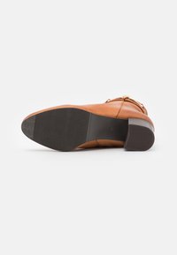 Botín de cuero marrón hasta el tobillo con un acabado suave, un tacón bajo tipo bloque y una suela de goma texturizada con ranuras verticales para mayor tracción.