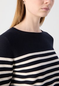 Navy kék pulóver vízszintes krém és világoskék csíkokkal, kerek nyakkivágással, texturált anyagból és formázott fazonnal.