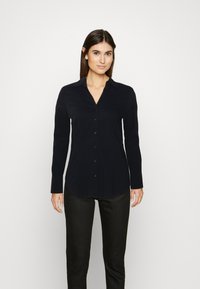 Zwarte lange mouwen shirt met een puntige kraag, knoopsluiting en een licht gebogen zoom. Draag het met donkere broeken, gladde stof structuur.