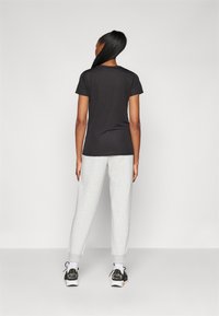 T-shirt noir à manches courtes, pantalon de jogging gris et chaussures de sport noires. Tissu lisse, coupe décontractée et poignets à la cheville sur le pantalon.