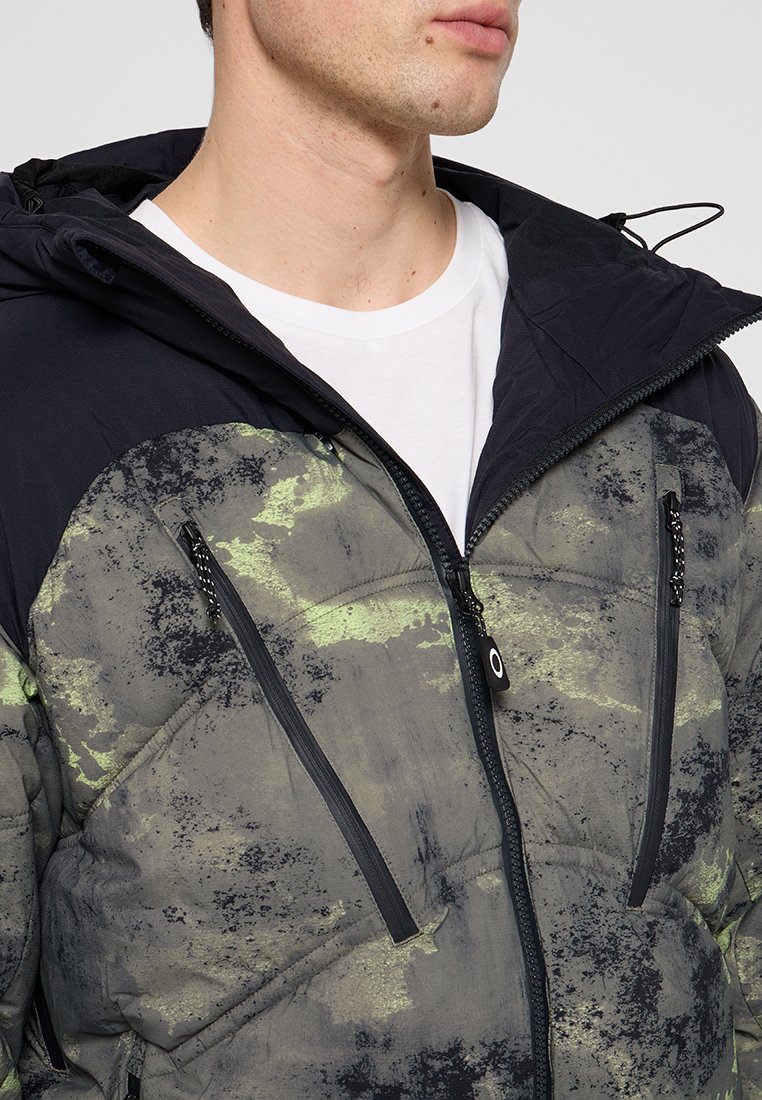 Veste rembourrée avec un motif texturé vert foncé et noir, dotée d'un col haut, de fermetures éclair à l'avant et de manches contrastées.