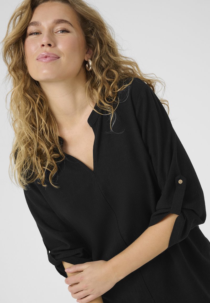 Camicia nera con colletto a V e maniche a tre quarti. Tessuto morbido con una leggera trama. Maniche arrotolate con dettagli a bottone.