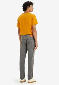 Jeans en denim gris avec une coupe droite et cinq poches. Associé à un t-shirt orange vif, avec un col rond classique.