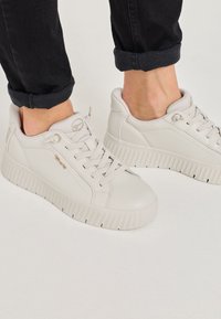Hellgraue Sneakers aus glattem Leder mit einer dicken strukturierten Sohle, runder Zehenpartie und flachen Schnürsenkeln. Mit einem Logo an der Seite akzentuiert.
