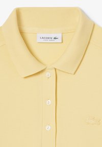 Polo shirt Lacoste slim fit jaune clair avec col, trois boutons et logo crocodile brodé sur la poitrine.