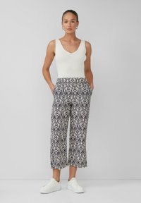 Biały podkoszulek z prążkowanej tkaniny, wzorzyste granatowe i kremowe szerokie spodnie w abstrakcyjny wzór liści, zestawione z białymi sneakersami.