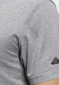 Szara teksturowana koszulka polo w kropki, z krótkim rękawem i czarnym logo na prawym ramieniu.