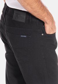 Les jeans en denim noir présentent un design classique avec des détails de couture visibles, une patch en cuir avec logo et des poches latérales.