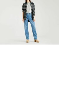 Camisa de franela a cuadros, camiseta gris, jeans de pierna recta de color azul claro y zapatos de plataforma beige. Entre las características se incluyen grandes bolsillos y mangas con puños.