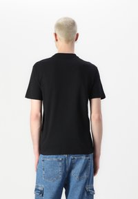 Black short-sleeve t-shirt made of soft fabric. Features a classic crew neck and relaxed fit, seen from the back against a white background.