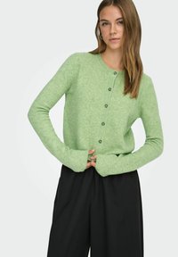 Hele-roheline pehme materjaliga kardigan, millel on ümmargune kaelus, nööpidega esikülg ja pikad varrukad soonikkoes mansettidega.