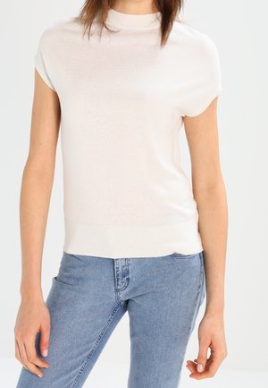 Light beige short-sleeve sweater with a high neckline. Soft knit fabric, fitted design, and a slightly ribbed hem detail. Paired with jeans.