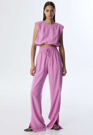 Twee-delig outift in felroze. Cropped mouwloos topje met ronde halslijn en wijde broekspijpen met een trekkoord in de taille en zijsplitten.