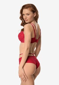 Czerwony koronkowy komplet bielizny z biustonoszem typu balkonette z regulowanymi ramiączkami oraz dopasowanymi przezroczystymi majtkami z kwiatowymi zdobieniami.