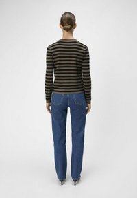 Gestreiftes Langarmoberteil in erdigen Braun- und Schwarztönen, kombiniert mit blauen high-waisted Jeans. Glatter Stoff, lockere Passform und spitze Absätze.