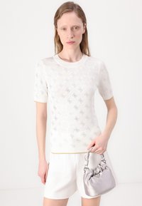 Top in maglia bianco a maniche corte con motivo floreale testurizzato, dettagli argento e rifiniture dorate. Abbinato a una piccola borsa in satin argento.