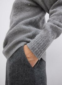 Maglione grigio lavorato a maglia con polsini a coste e decorazioni sparse, abbinato a pantaloni grigi a spina di pesce con tasche laterali.