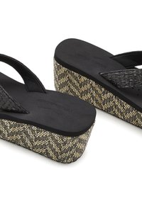 Black flip-flops with woven straps, featuring a wedge sole with a textured black and beige zigzag pattern. Durable material and design for comfort.