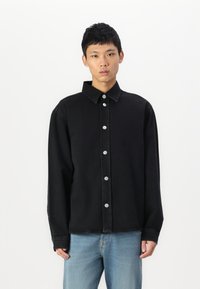 Camisa de mezclilla negra con cuello tipo camisa, cierre frontal de botones en acero inoxidable y mangas largas, con un corte relajado y una textura suave.