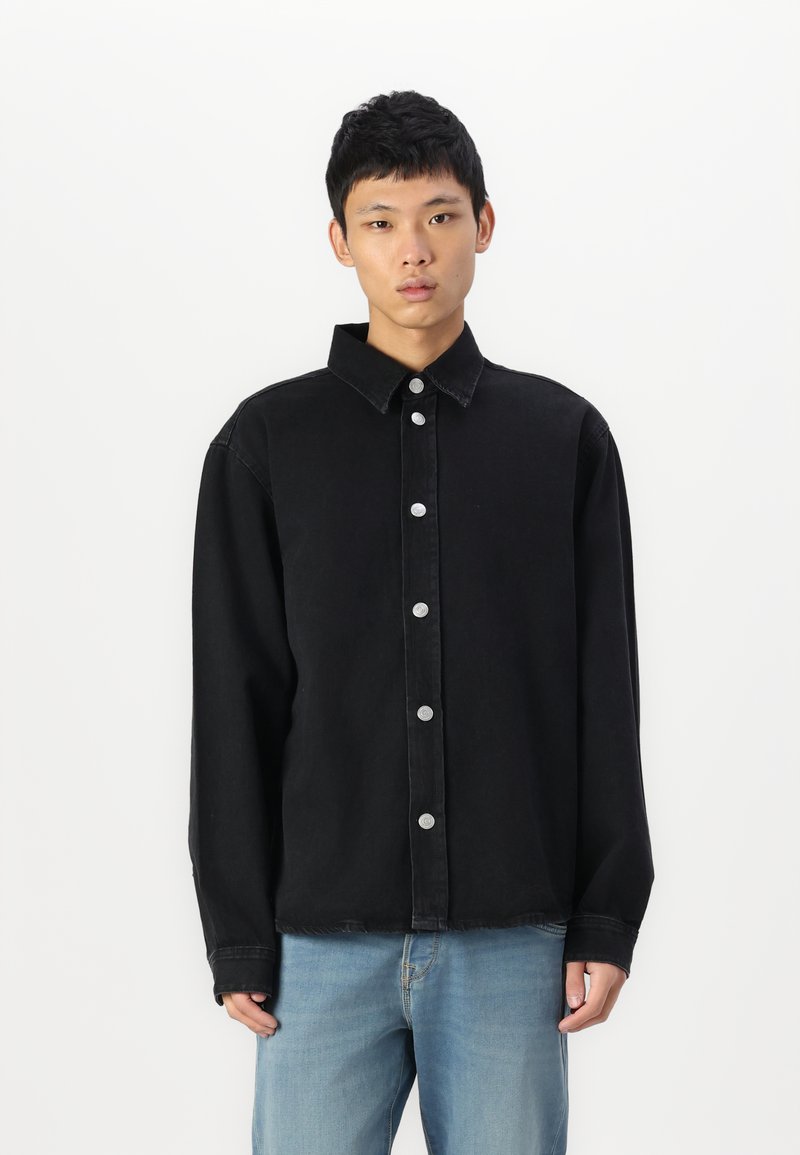 Camisa de mezclilla negra con cuello tipo camisa, cierre frontal de botones en acero inoxidable y mangas largas, con un corte relajado y una textura suave.