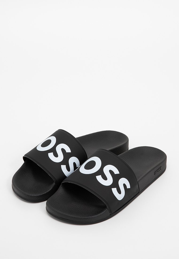 Des sandales noires à glissière avec une large sangle portant le mot "BOSS" en bleu clair. Semelle intérieure texturée et semelle extérieure en caoutchouc pour une bonne adhérence.