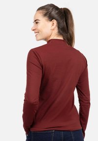 Burgundia värvi pika varrukaga figureeriv pluus, millel on kõrge kaelus ja siidine tekstuur, ühendatud tumeliste siniste teksadega.