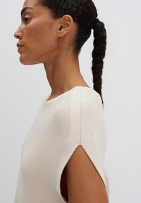 Maglietta a maniche corte color crema in maglia con dettagli testurizzati sulle spalle e fessure laterali. Materiale morbido e leggero con una vestibilità rilassata.