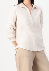 Light beige button-up shirt made of textured linen, featuring two chest pockets and rolled-up sleeves for a relaxed fit.