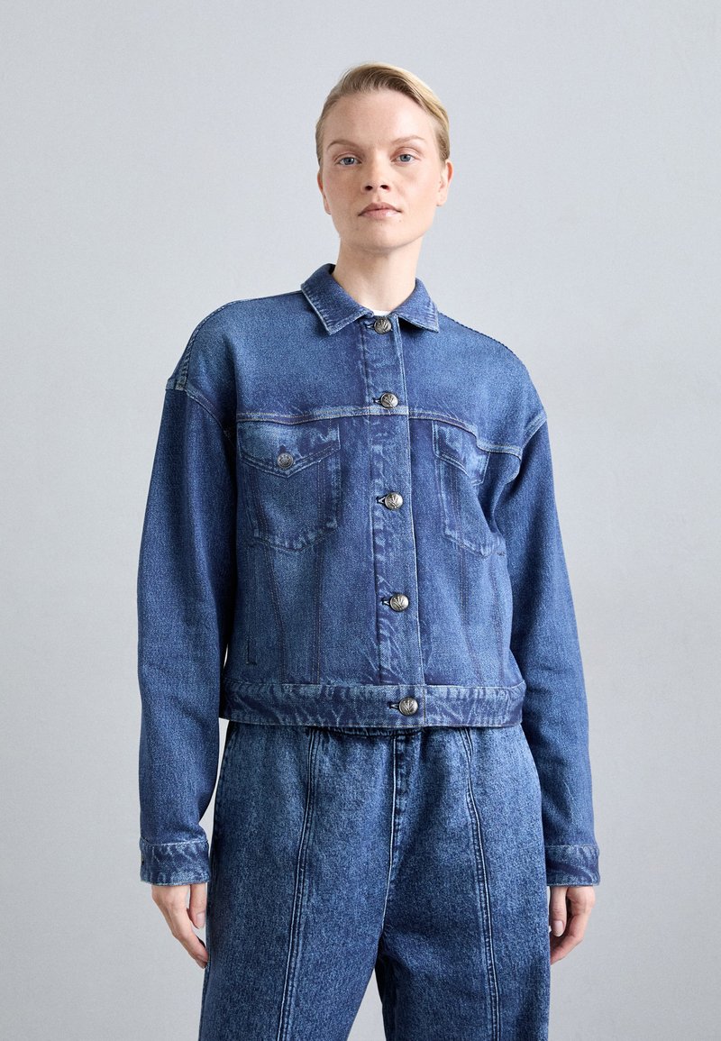 Jachetă din denim albastru cu guler, închidere cu nasturi în față, două buzunare la piept și un design scurt. Textură moale și finisaj estompat.