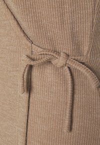 Maglione lavorato a maglia in una morbida tonalità di marrone con una texture a costine. Presenta un dettaglio in vita legato e una finitura laterale.