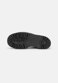 Black rubber shoe sole featuring a thick tread pattern, with grooves and angles for traction. Textured surface with logo detail.