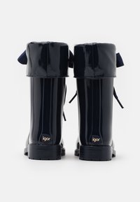 Bottes de pluie en caoutchouc bleu marine avec une finition brillante, présentant un haut arrondi, deux nœuds décoratifs et une semelle noire robuste avec un détail de logo.