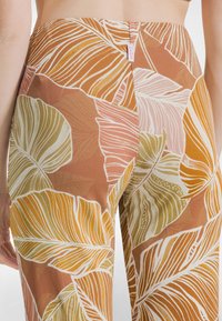 Wzorzyste spodnie z dużymi, wielokolorowymi tropikalnymi liśćmi w odcieniach pomarańczu, zieleni i bieli; gładka tkanina o dopasowanym kroju.