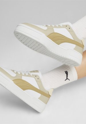 Sneakers beige e bianche con una texture liscia, caratterizzati da un design a strati, accentuato da una striscia beige e una suola bianca spessa.