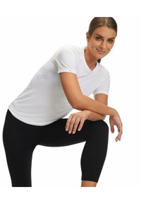 T-shirt atletico bianco con maniche corte e scollatura rotonda. Indossato con leggings neri. Presenta un pannello laterale testurizzato e un dettaglio del logo.