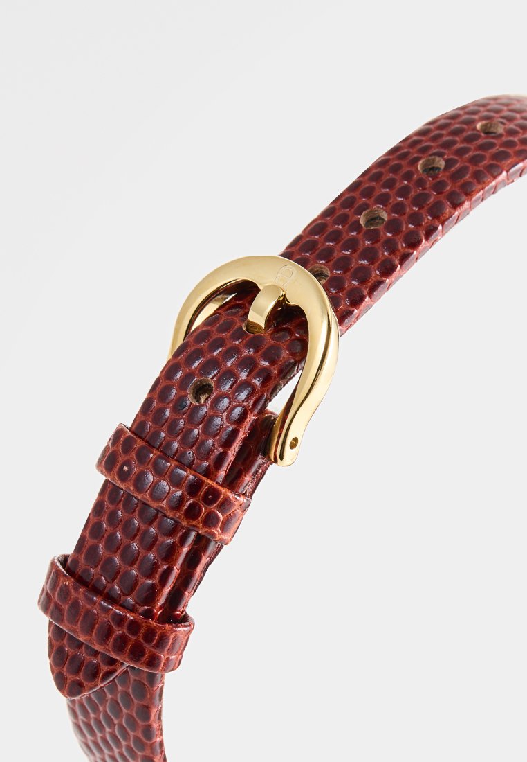 Bracelet de montre en cuir texturé rouge avec boucle dorée et trous ajustables, mettant en valeur une surface distinctement en relief.