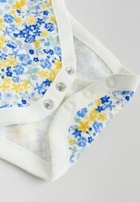Bodysuit s cvjetnim uzorkom s plavim, žutim i zelenim cvjetovima na bijeloj podlozi. Ima tri srebrna kopčanja i bijelu obrubu.