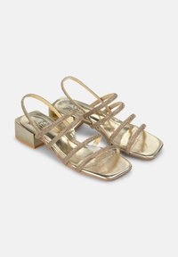 Gouden metallic sandalen met meerdere dunne banden, vierkante neus en een korte blokhak. Heeft een gladde textuur en een glanzende afwerking.