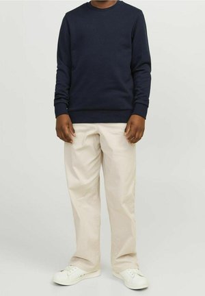 Námořnická mikina s kulatým výstřihem a žebrovanými manžetami, v kombinaci s světle béžovými kalhotami a bílými teniskami, stojící před neutrálním pozadím.