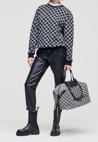 Sweter w biało-czarny wzór houndstooth, czarne skórzane spodnie, czarne botki za kostkę oraz szara torba duffle z czarnymi akcentami i metką z logo.