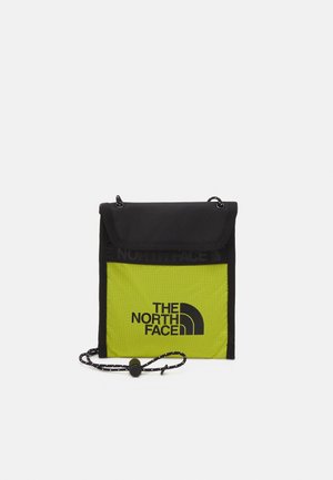 Petit sac bandoulière noir et jaune fluo avec le logo The North Face et une sangle cordon réglable avec un toggle noir.