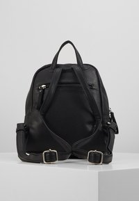Sac à dos en cuir texturé noir avec des bretelles ajustables, des accessoires en argent et une poche zippée à l'avant. Présente une silhouette structurée.