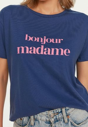 Marineblaues T-Shirt mit pinkem Schriftzug "bonjour madame," getragen zu hellblauen Jeans von einer Person, die vom Hals bis zur Taille zu sehen ist.