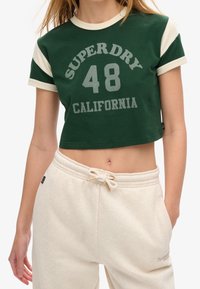 Grøn cropped t-shirt med cremefarvede ærmer, der har teksten "SUPERDRY 48 CALIFORNIA" i grå. Sættet er parret med cremefarvede sweatpants med snoretræk.