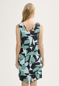 Mouwloze jurk met een V-rug, voorzien van een veelkleurig abstract patroon in teal, groen en marineblauw op een lichte achtergrond.